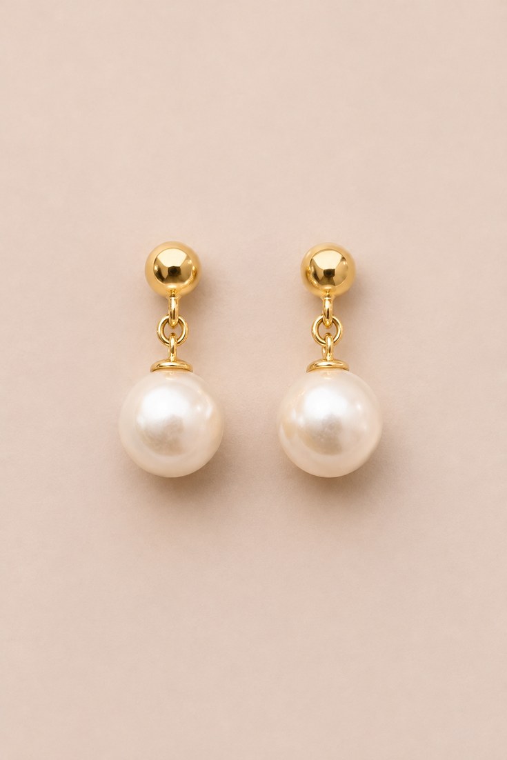 A pair of pearl drop earrings with gold links on a champagne backdrop