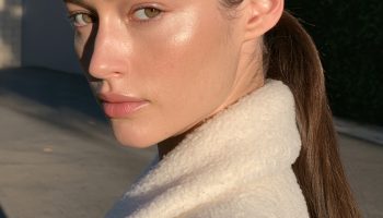 Woman with glossy espresso brown hair in a sleek low ponytail wearing a cream coat