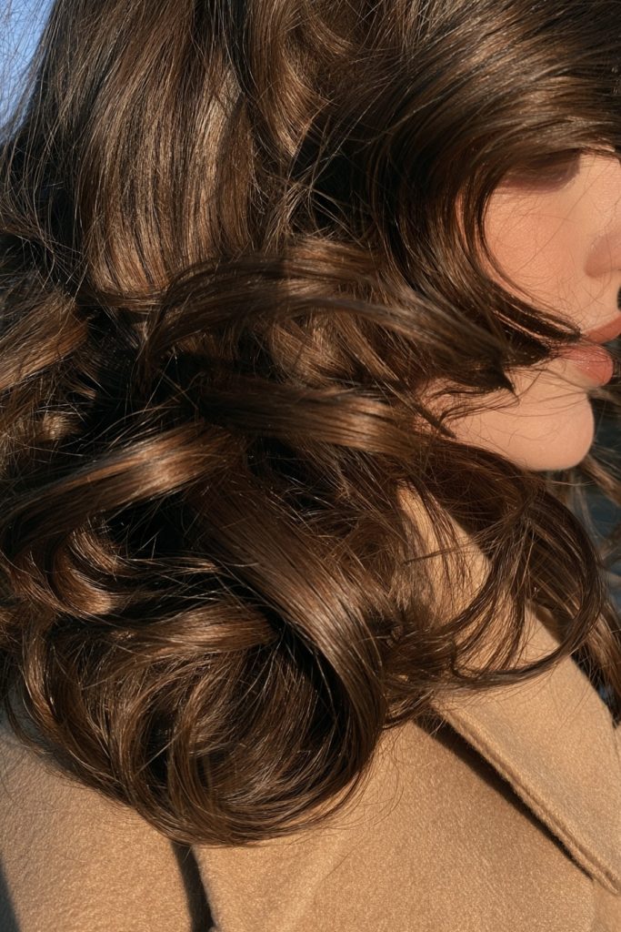 Close up of rich espresso brown soft curls over the shoulder of a camel coat