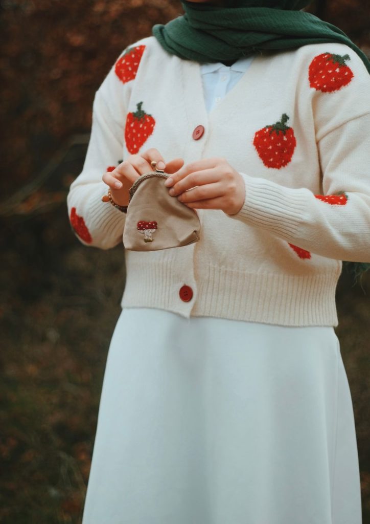 White cardigan with red strawberry embroidery and red buttons over a white skirt