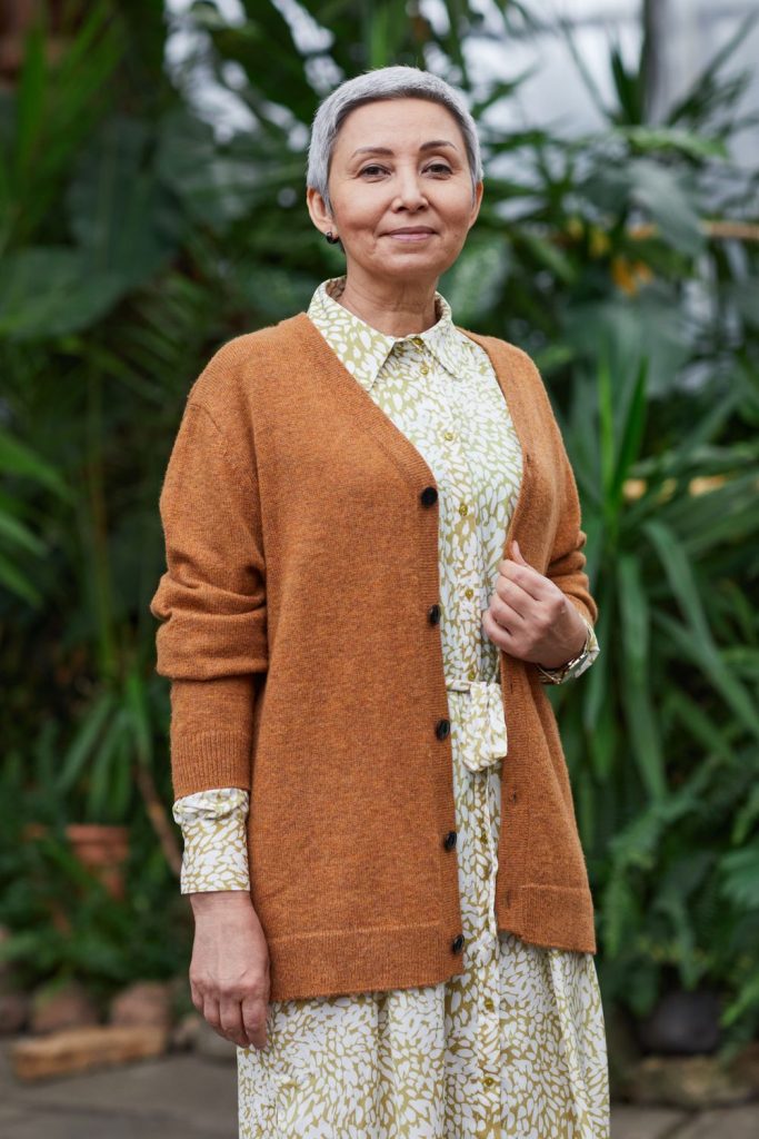 Mature woman in a rust orange button cardigan over a collared floral shirt dress