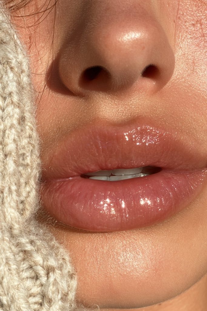 Close up of lips with a sheer caramel lip gloss beside a cozy knit sleeve