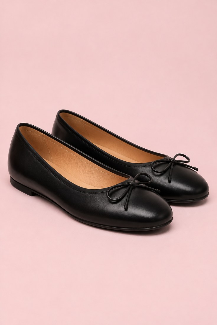 Black leather round toe ballet flats with a thin bow on a soft pink background