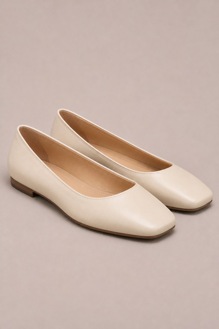 Pair of cream leather square toe ballet flats on a pale taupe background