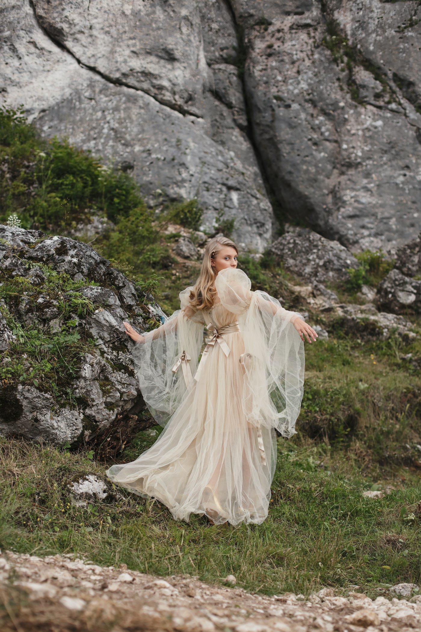 Woman in a flowing gown standing in a rocky landscape
