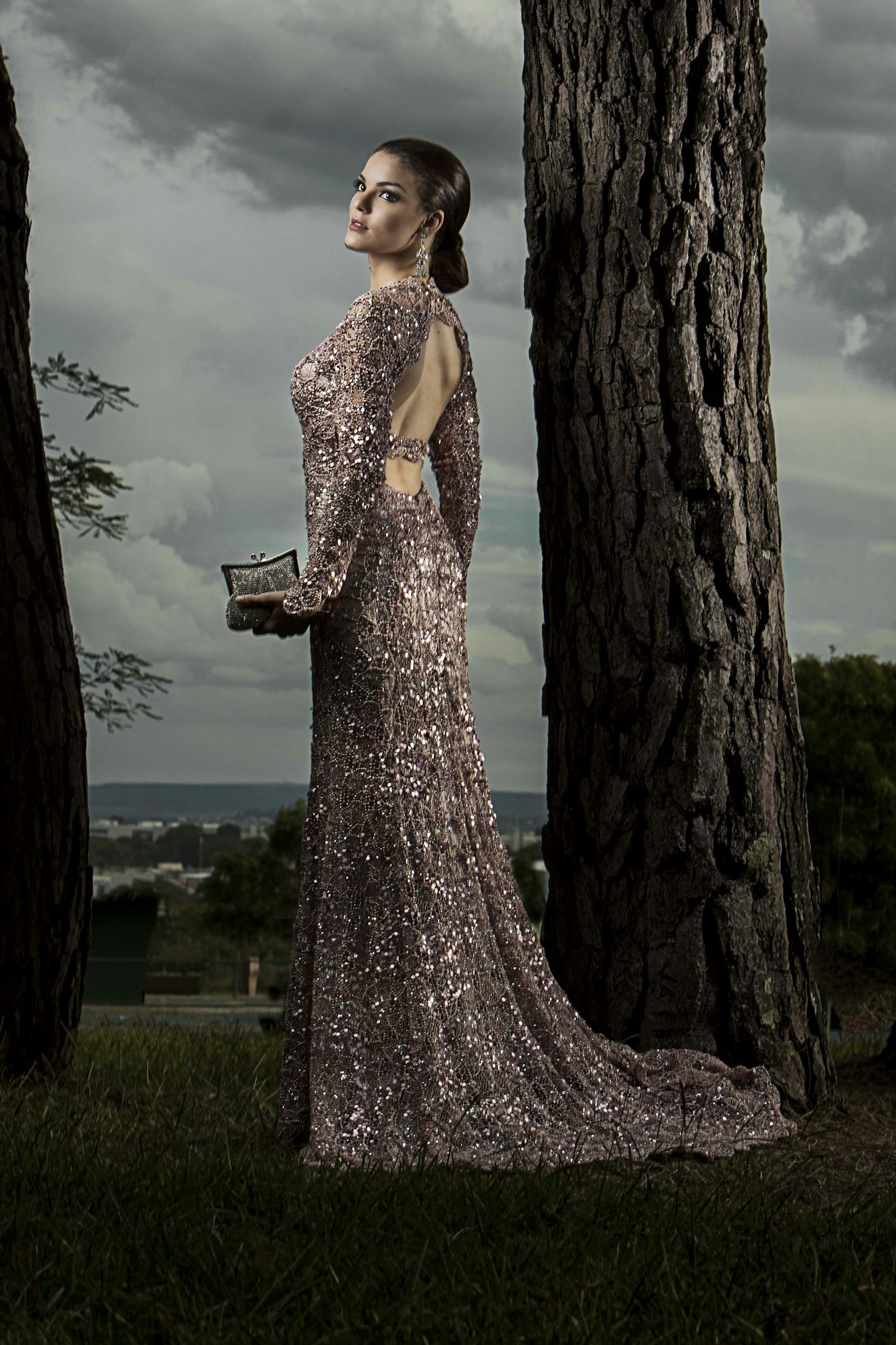 Woman in a gray glitter gown standing beside a tree