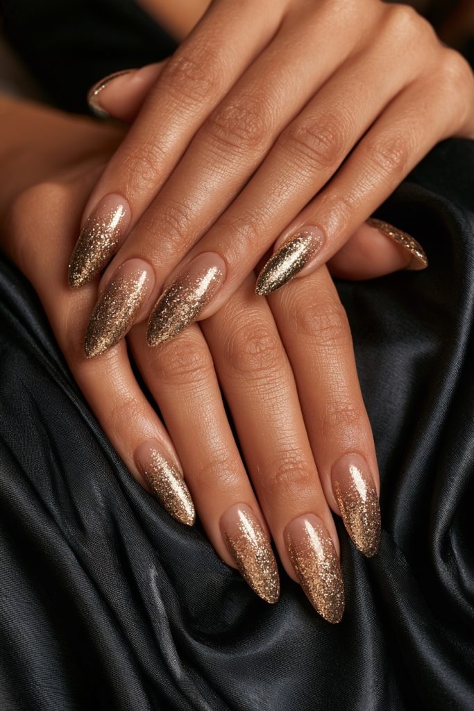 Close up of hands with almond gold glitter ombre nails resting on black satin
