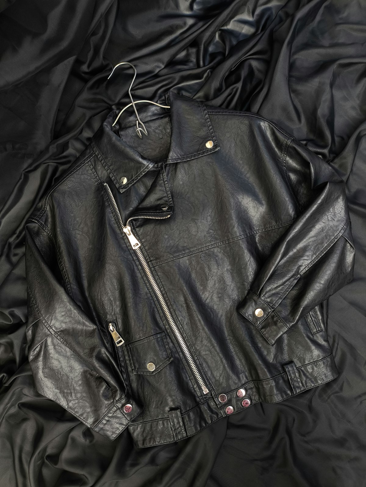 Cropped black leather jacket laid flat on a bed
