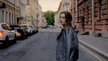 Woman in a black leather jacket on a city street, styled for a leather jacket and jeans outfit