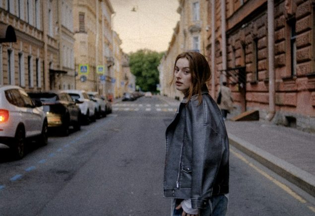 Woman in a black leather jacket on a city street, styled for a leather jacket and jeans outfit
