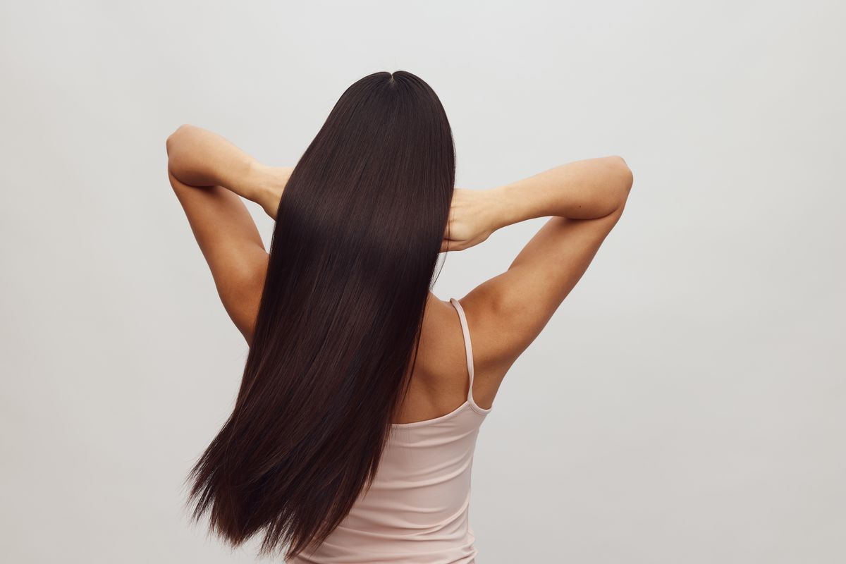 Woman seen from behind with very long, straight dark hair, her hands raised behind her head