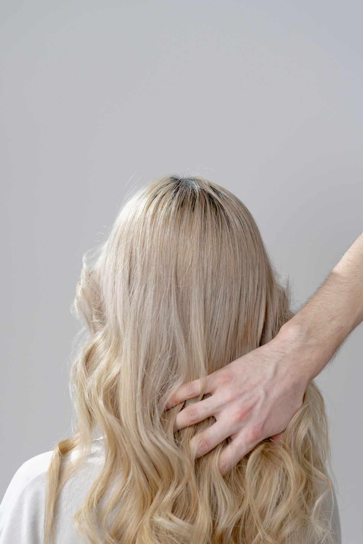 Blonde hair seen from behind with a hand lifting a section near the ends