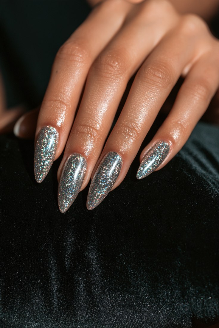 Holographic glitter nails sparkling on a hand resting on a black velvet cushion
