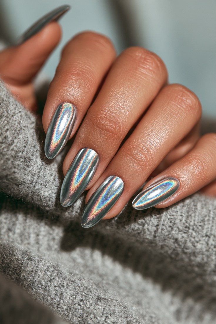 Mirror holographic chrome powder nails on a hand resting on a grey cashmere sweater