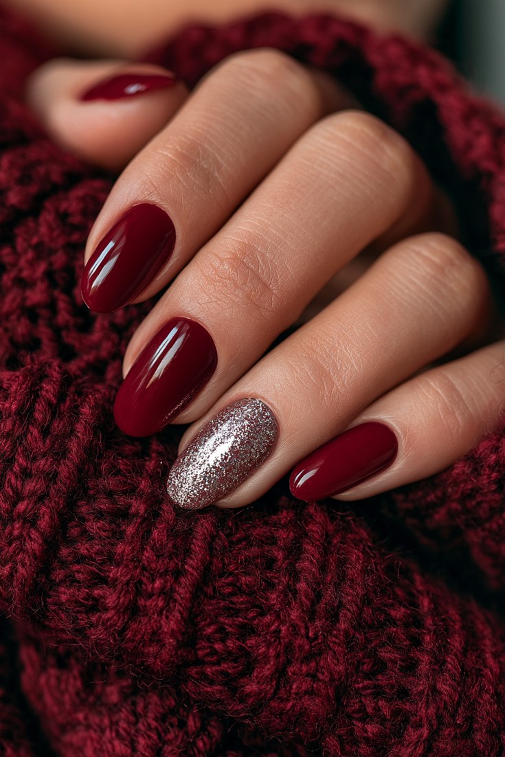 Dark red nails with one holographic accent nail on a hand resting on a burgundy wool scarf