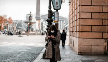 Woman in a black coat and black trousers on a city sidewalk, styled for a trench coat and wide leg trousers outfit