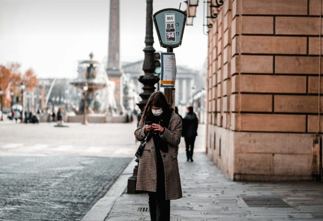 Woman in a black coat and black trousers on a city sidewalk, styled for a trench coat and wide leg trousers outfit