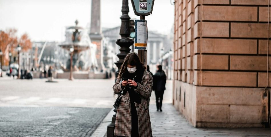 Woman in a black coat and black trousers on a city sidewalk, styled for a trench coat and wide leg trousers outfit