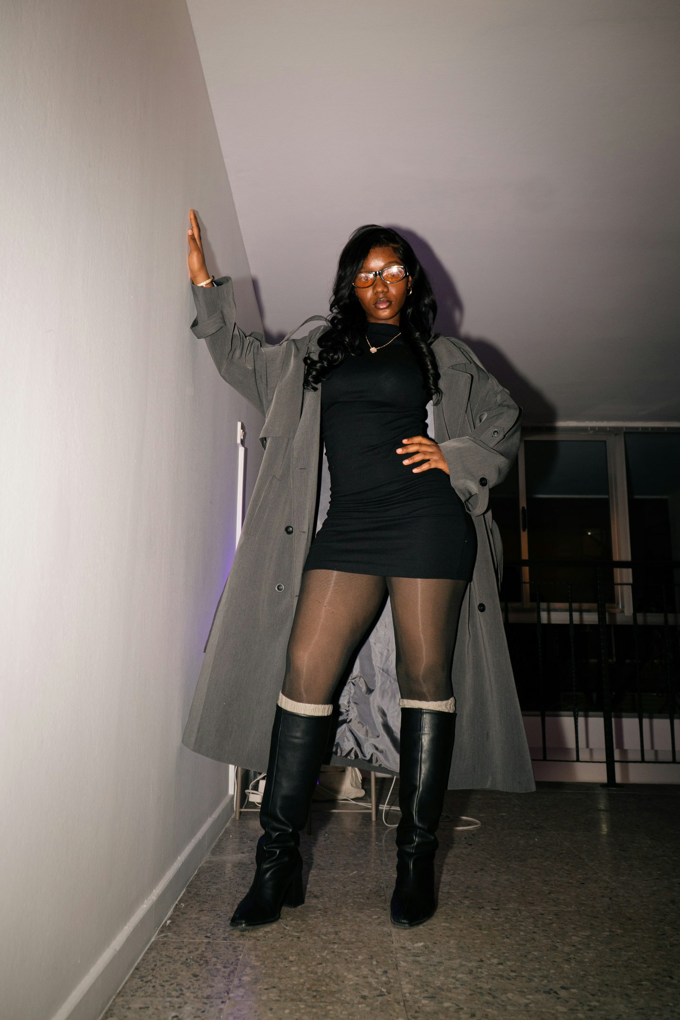 Woman in a trench coat and boots leaning on a wall