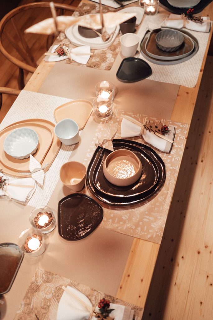 Dinner table covered with a brown kraft paper runner, handmade ceramic plates, bowls and small candles