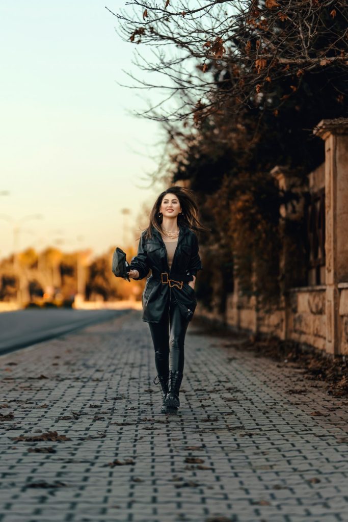 Woman walking down a cobblestone street at sunset in a black leather jacket, black leather trousers and a belt