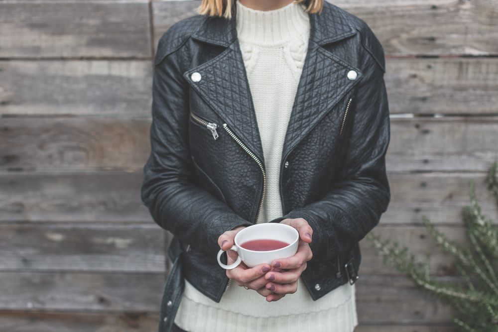 Close-up of a black quilted leather biker jacket over a chunky white turtleneck holding a cup of tea