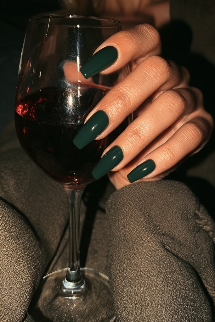 Close up of hands with long dark green nails holding a glass of red wine