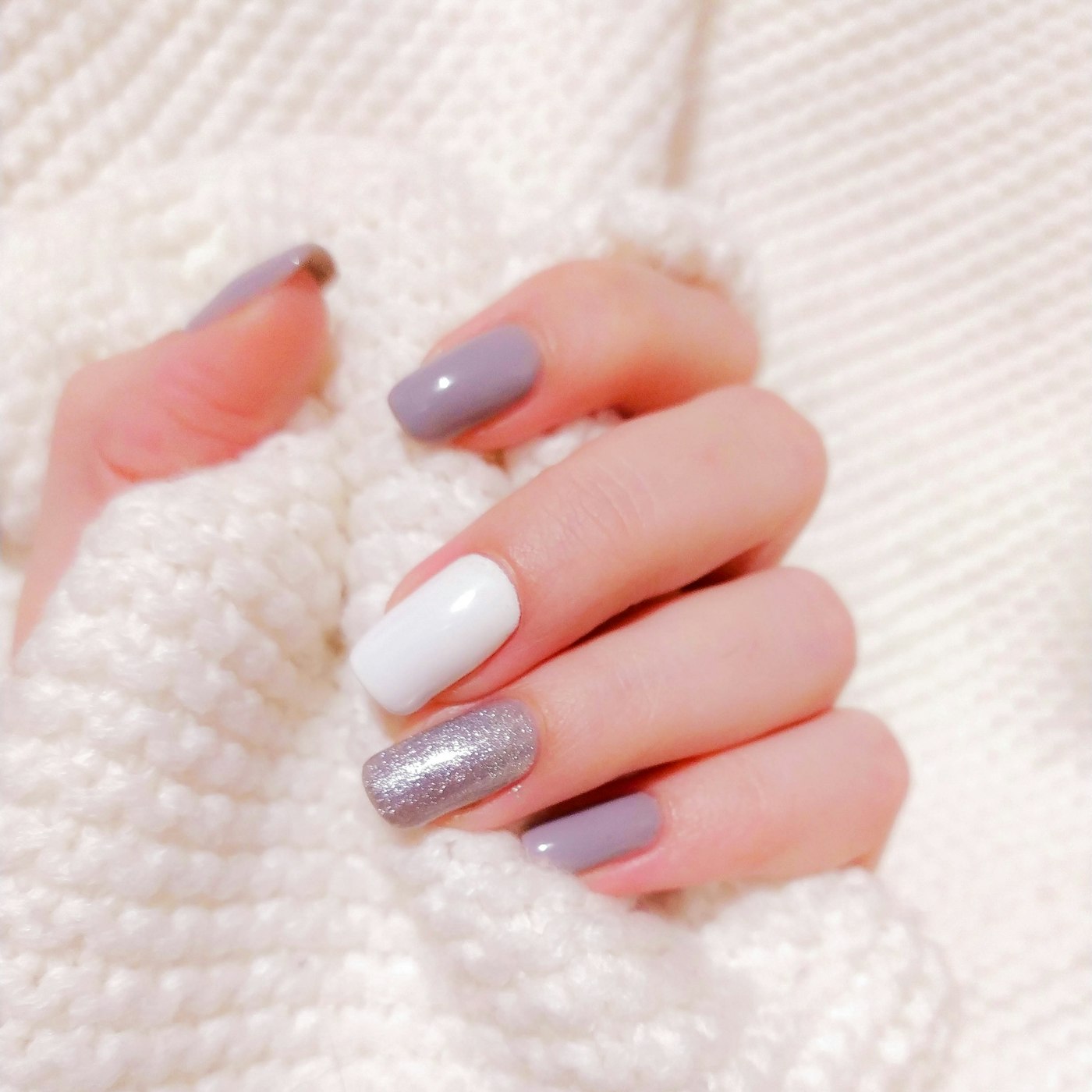Hand with mauve, white and silver glitter nails holding a white knit sweater