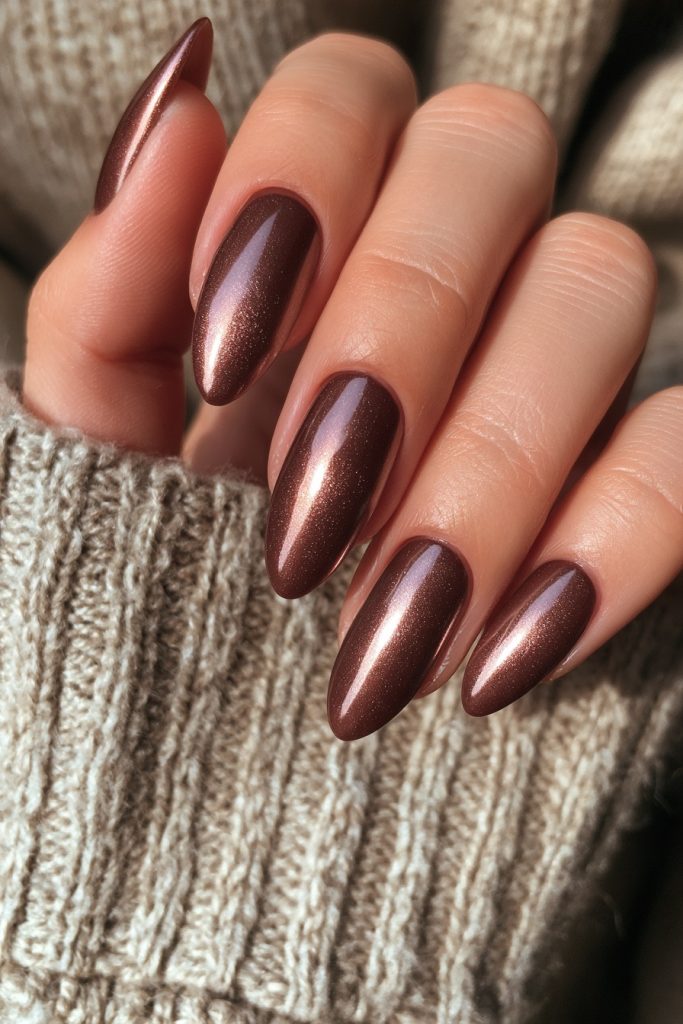 Hand with long almond nails in deep mocha brown with a copper shimmer resting on a beige ribbed knit sweater