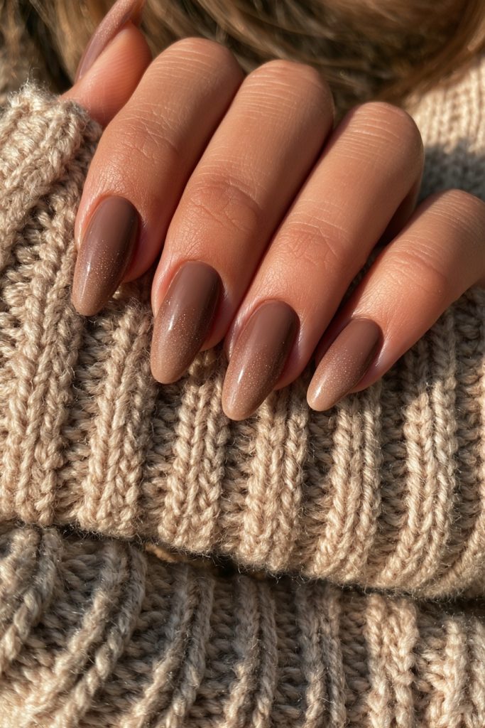 Hand with glossy mocha brown almond nails resting on a beige ribbed knit sweater