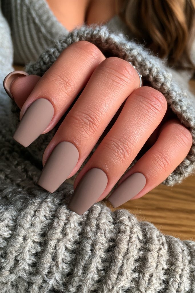 Hand with long matte taupe mocha coffin nails resting on a grey ribbed knit sweater