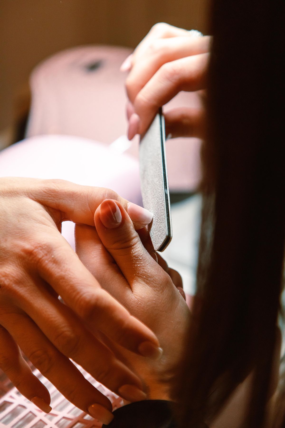 Close-up of a hand having a nail filed with a file held against the fingertip