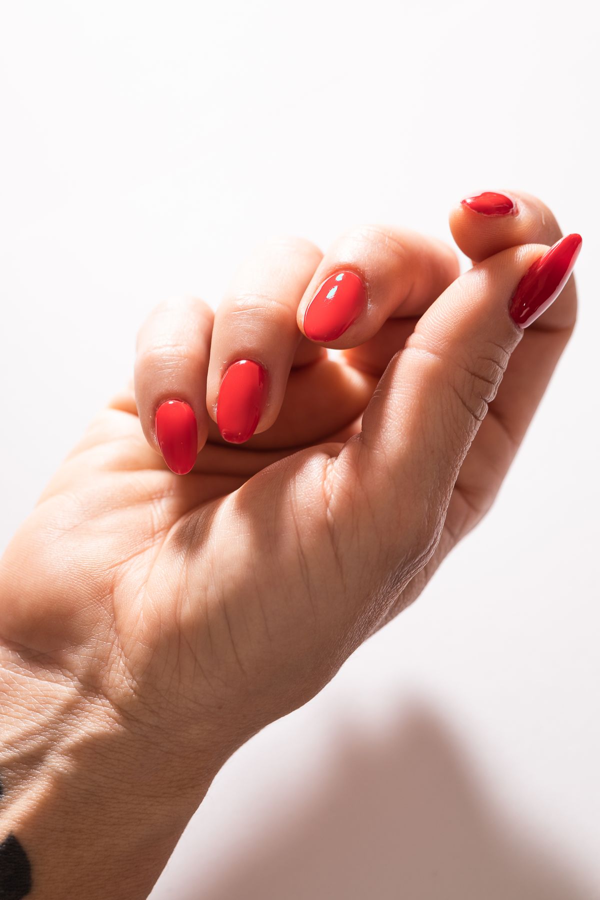 Two hands with short glossy red nails touching at the fingertips