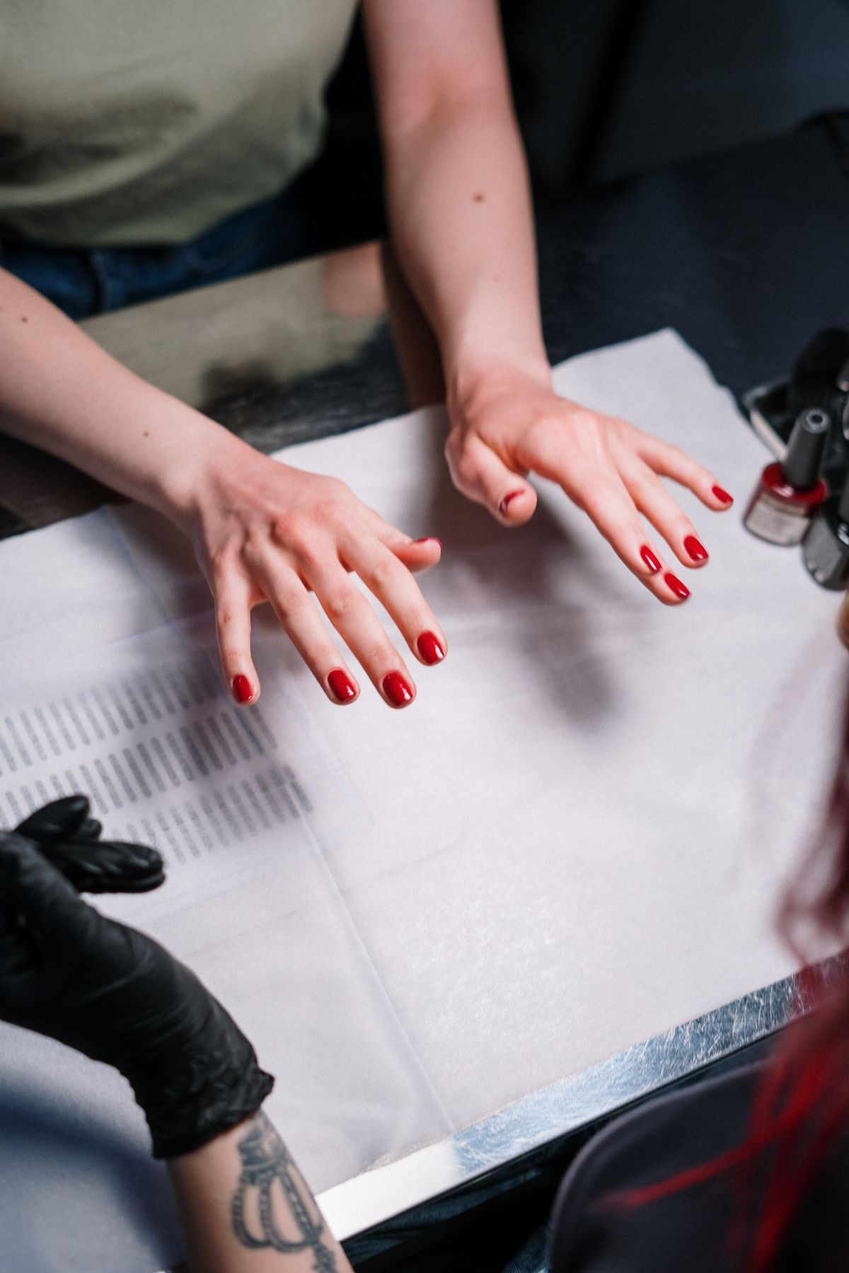 Salon table with two hands resting on a white towel, both showing red painted nails