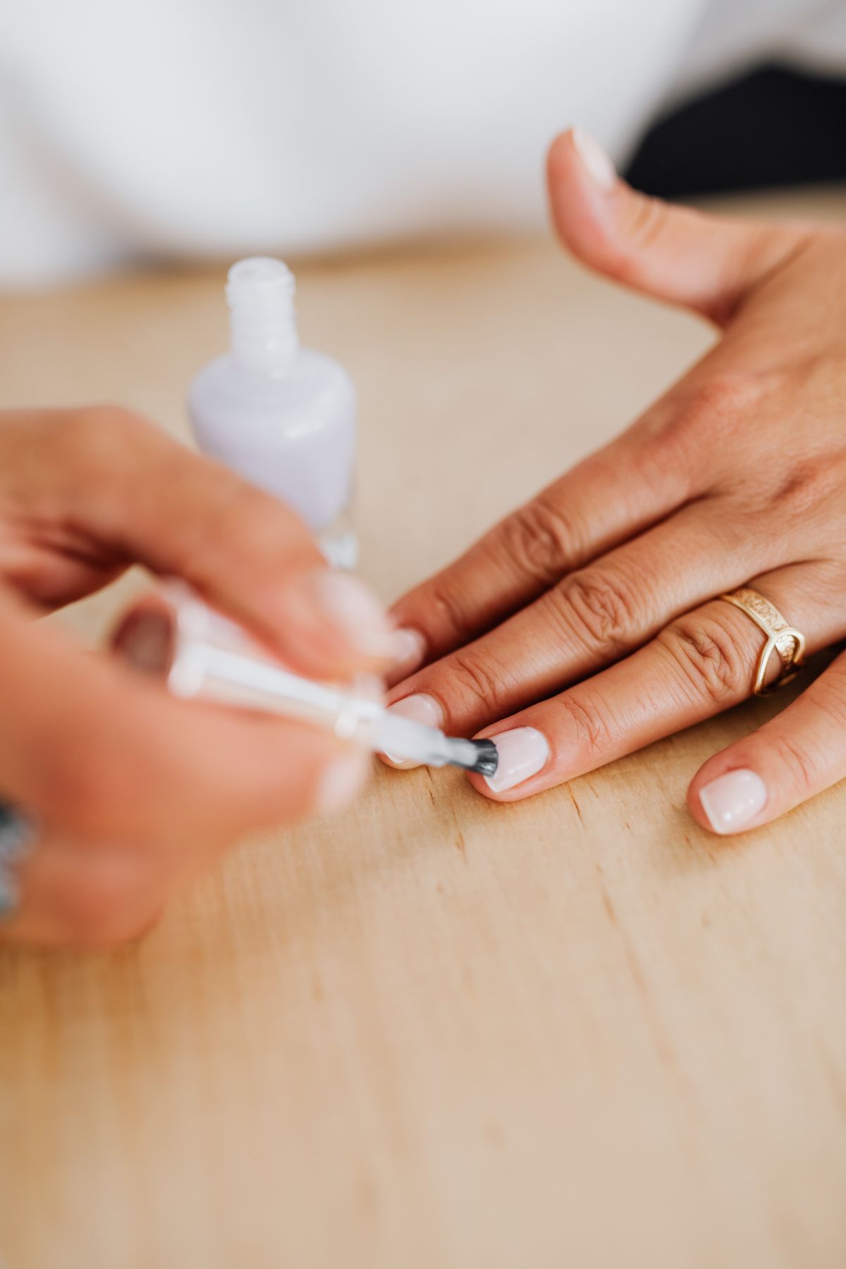 Hand with a ring on one finger as a brush applies a pale polish to a nude nail