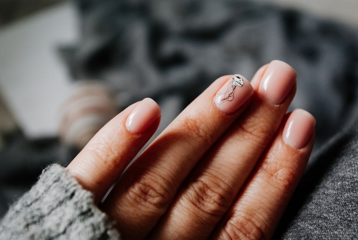 Hand with short, natural, pale pink nails resting on a grey knit surface