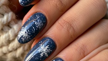 Close-up of a hand with glossy navy blue almond nails with white snowflake designs on a chunky cream knit