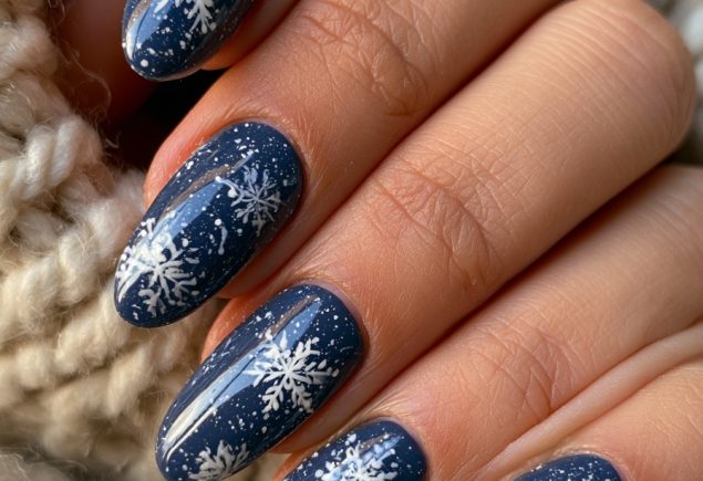 Close-up of a hand with glossy navy blue almond nails with white snowflake designs on a chunky cream knit