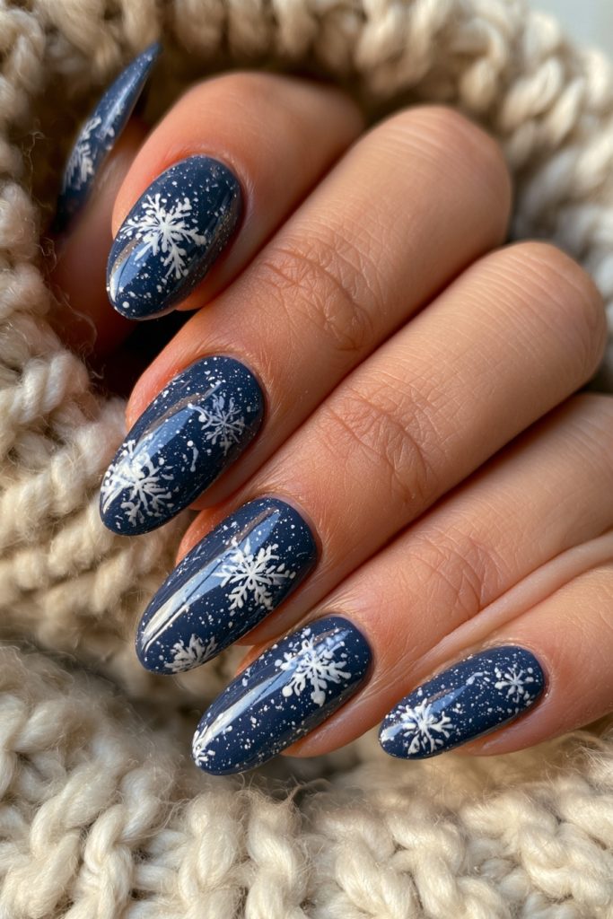 Close-up of a hand with glossy navy blue almond nails with white snowflake designs on a chunky cream knit