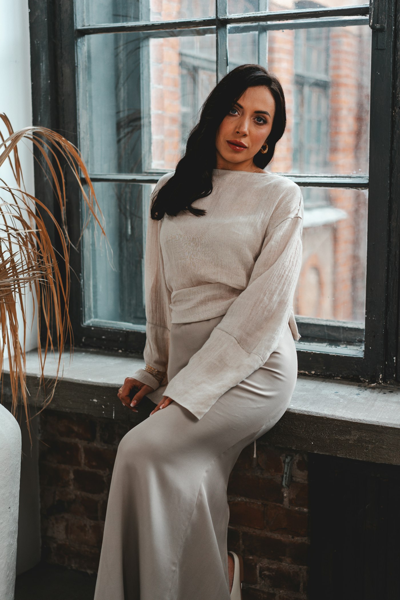 Woman posing by a window in a soft neutral dress