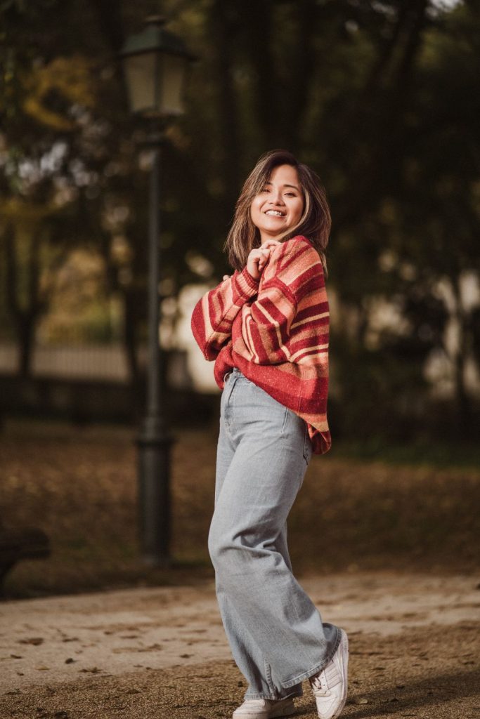 Woman smiling in a park in a red and cream striped sweater and wide-leg grey trousers