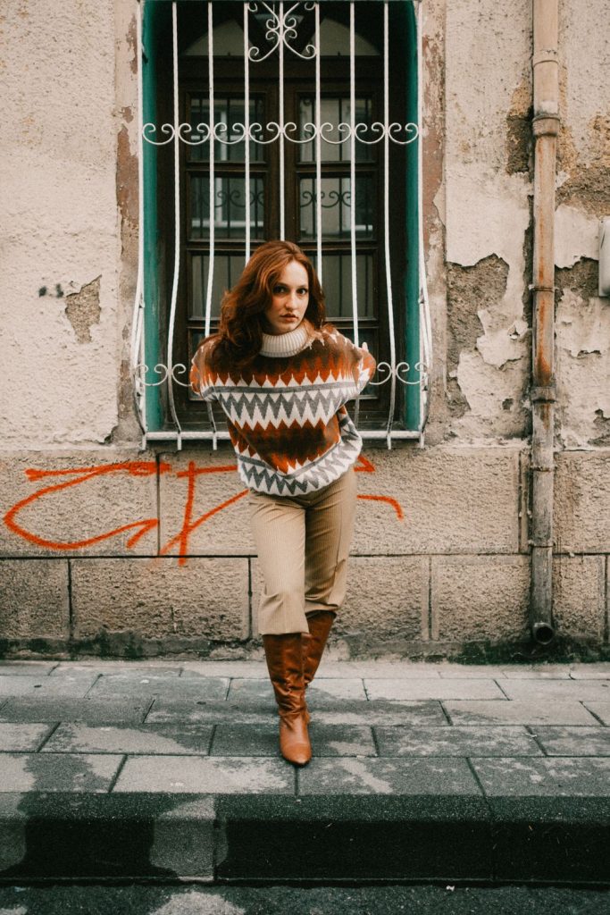 Woman in a brown and white patterned knit sweater with camel trousers and tan boots in front of a graffiti wall