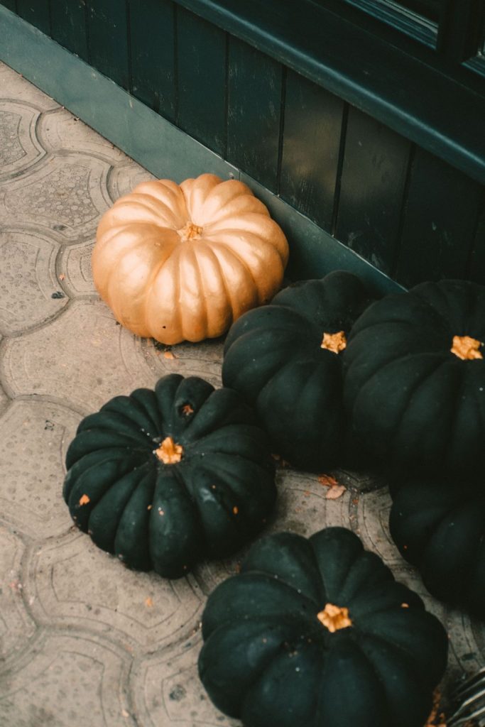 A copper toned pumpkin among deep green pumpkins grouped on a patterned tile floor for fall decor