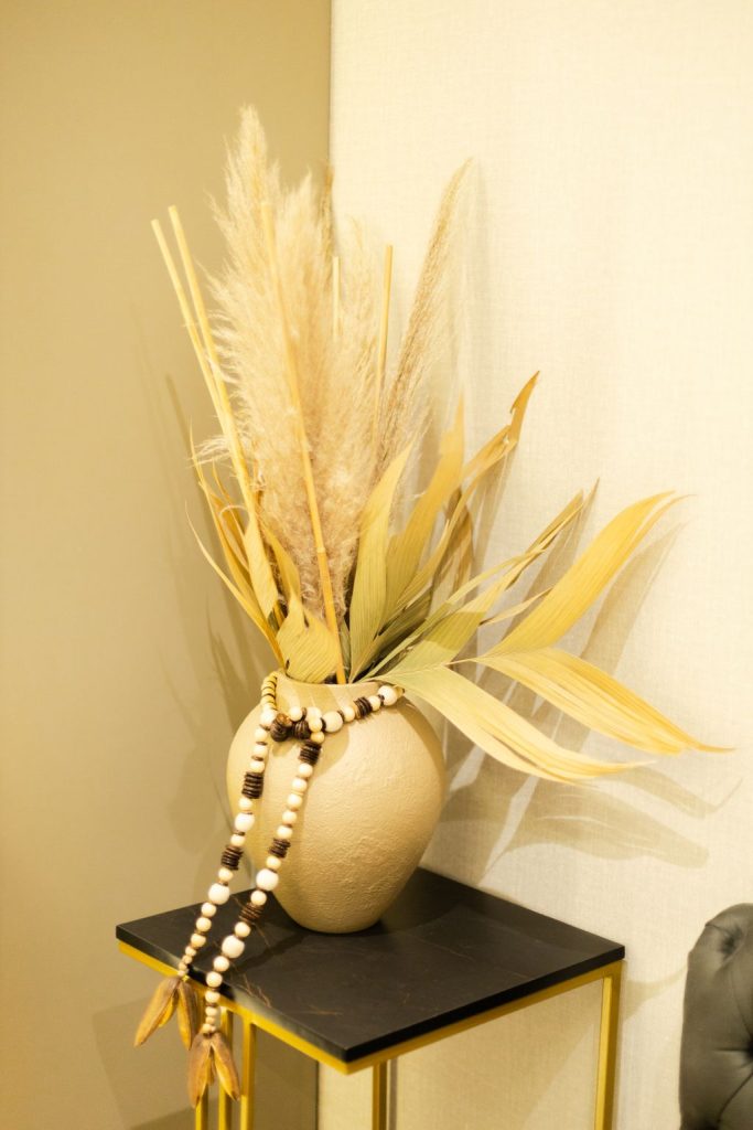 Cream pampas grass and dried stems in a ceramic vase with a wood bead garland draped over a side table