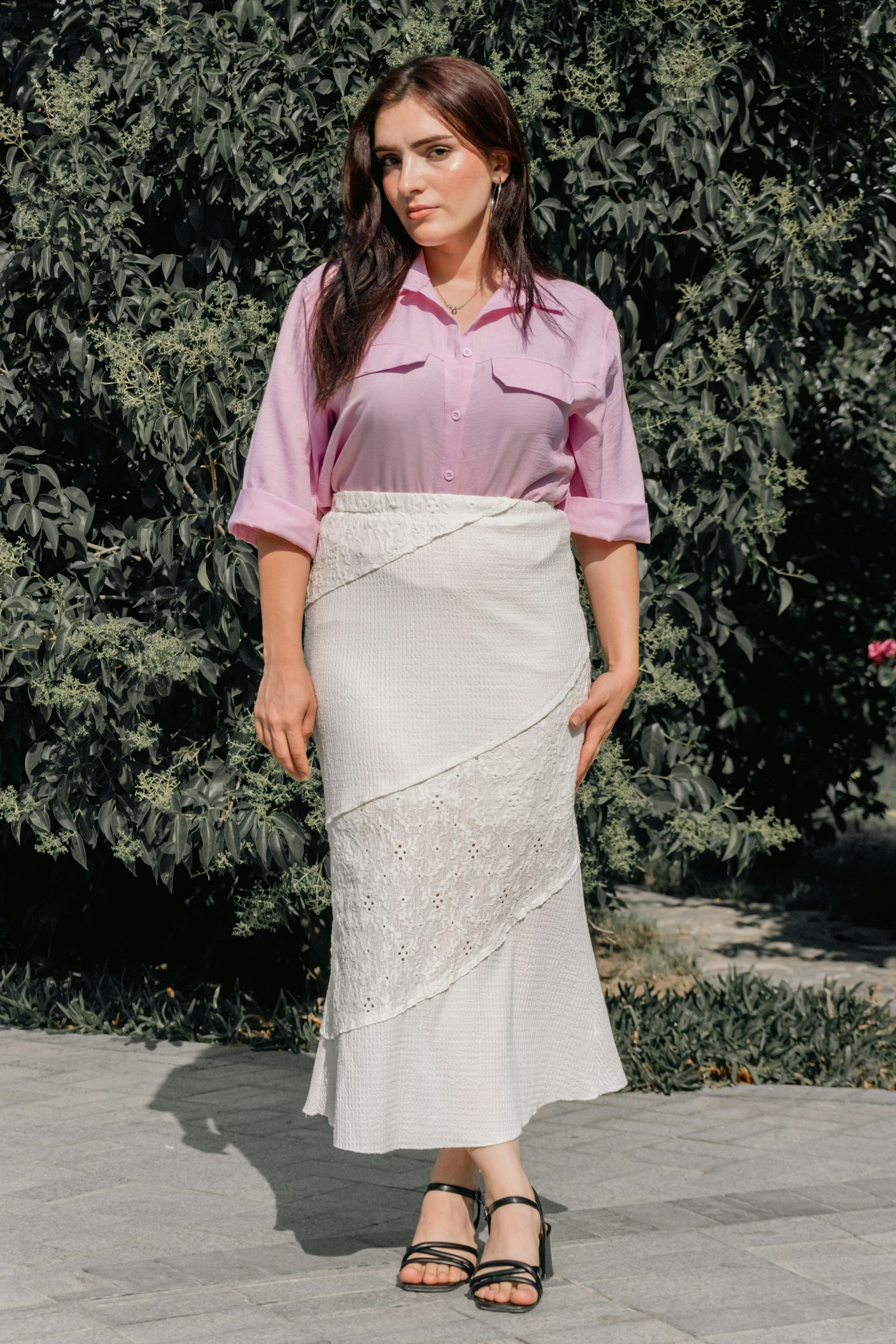 Woman in a soft pink top and white skirt in front of greenery