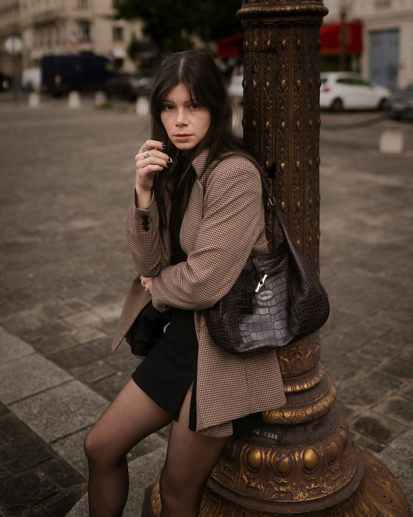 Woman in a plaid blazer and black skirt leaning against an ornate lamppost