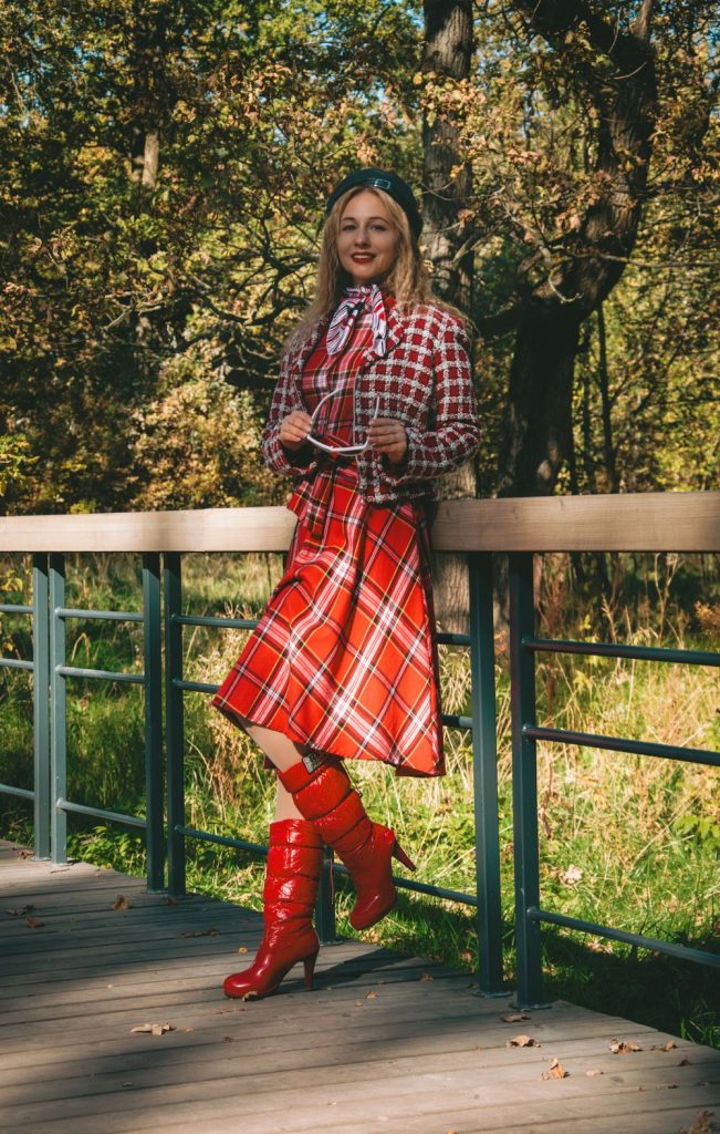 Woman in a red plaid shirt, a long red plaid skirt and red boots standing on a bridge in autumn