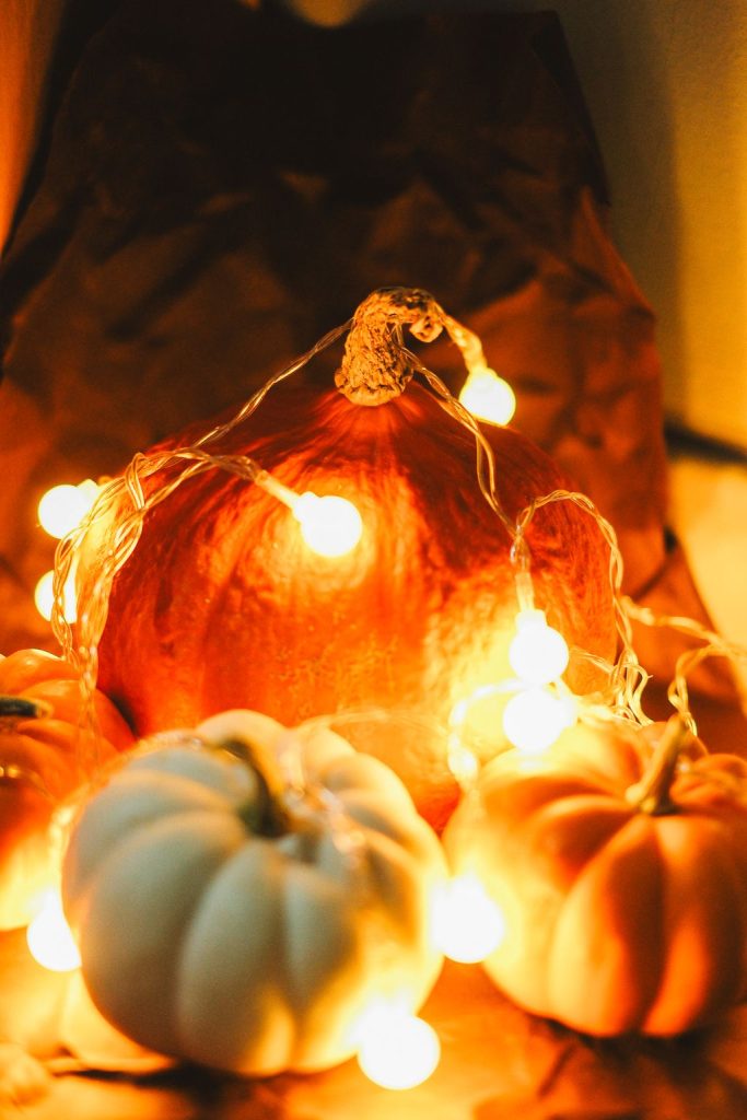 Orange and white pumpkins wrapped in glowing warm string lights, a simple cozy autumn decoration