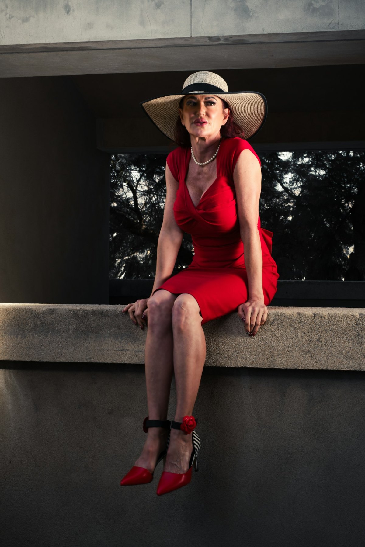 Woman in a red dress and hat sitting on a ledge