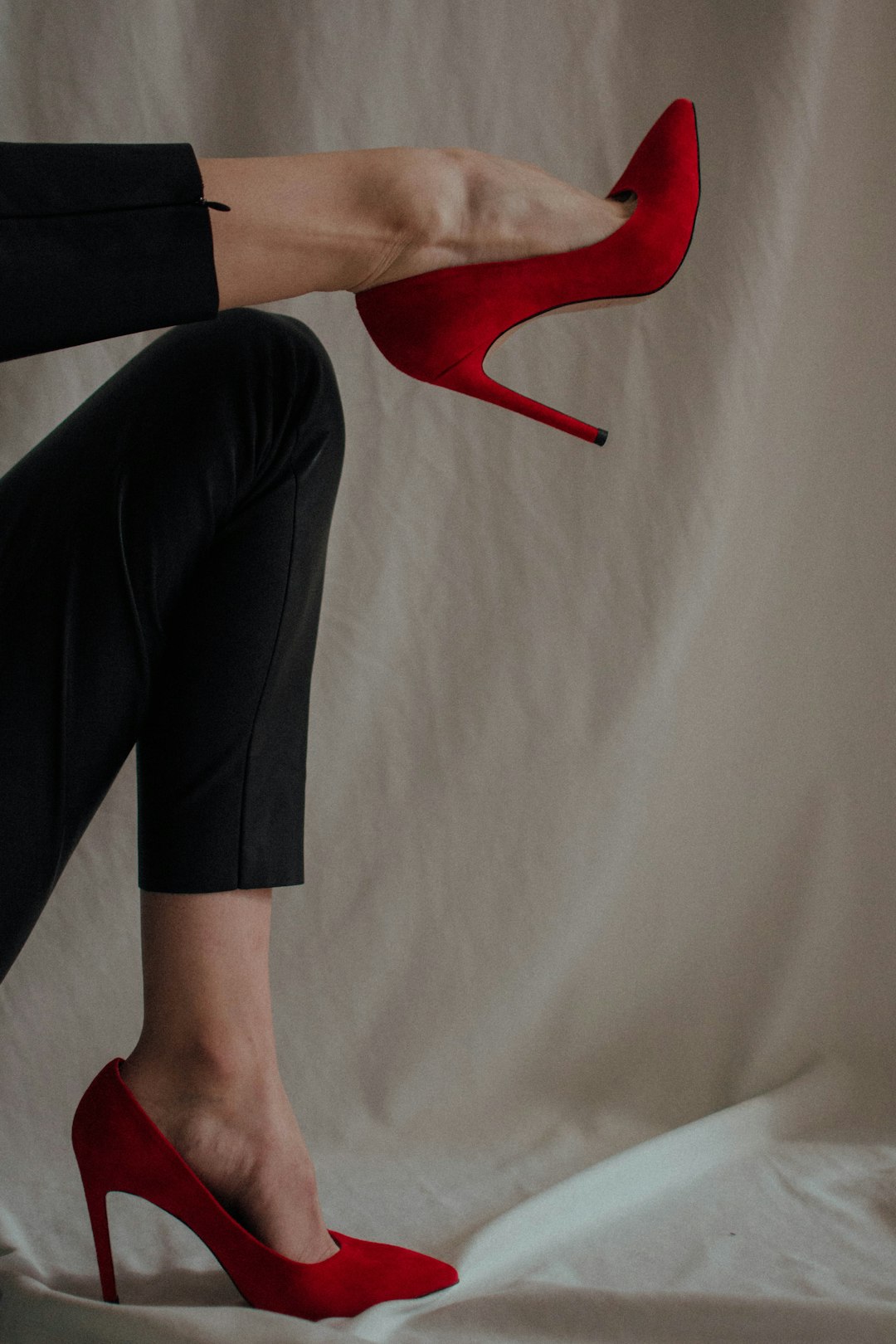 Person in black trousers and red shoes standing on a light surface